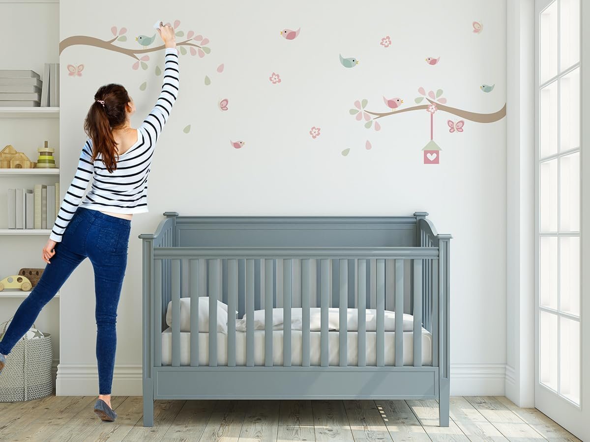 Mulher decorando parede de quarto com adesivo de parede infantil galhos e pássaros passarinhos.
